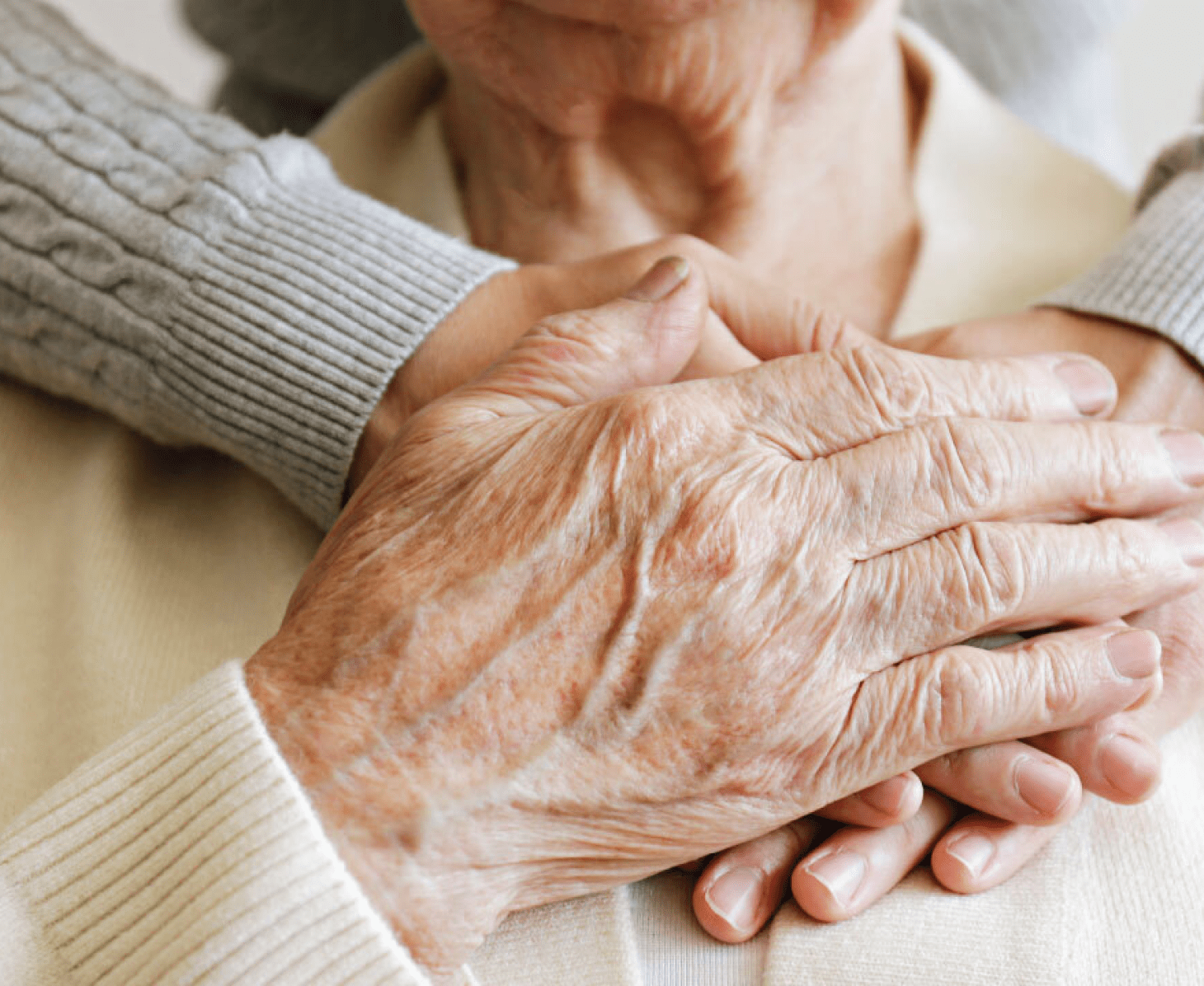 close up of old couples hands - the woman's hand is placed over the mans hand.